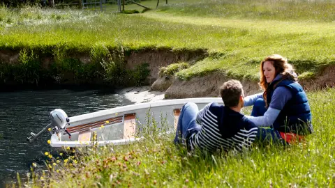 Douze personnes assises sur une rive à côté d’un bateau dans l’eau.